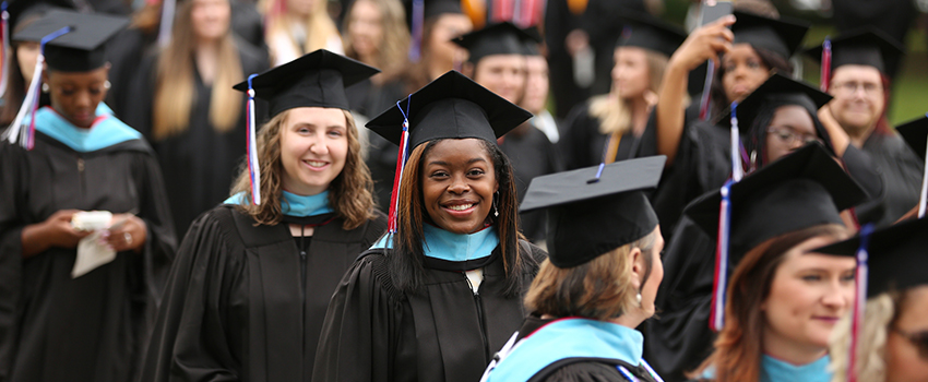 African American Female graduate smiling in cap and gown walking in a line to graduation.