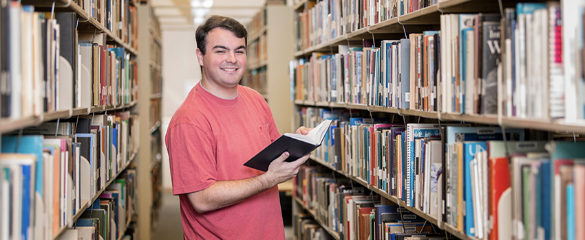 Male student holding a book in the library.