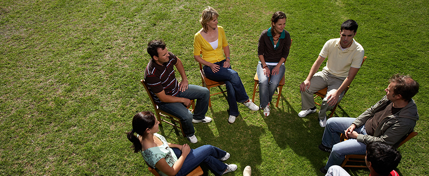 A group of people sitting in chairs in a circle outside talking.