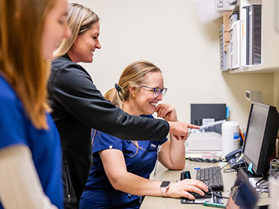 Three women in scrubs looking a computer screen.