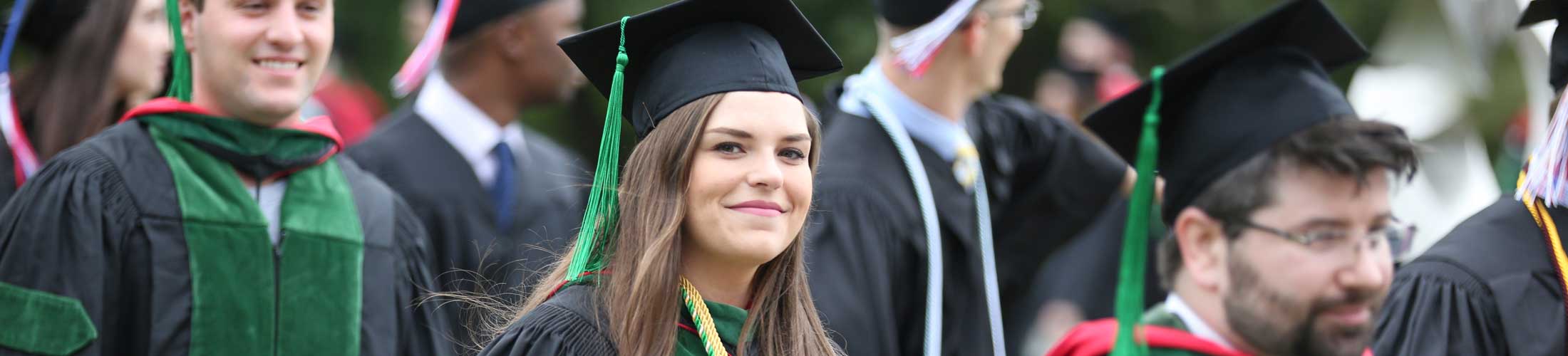 Graduate smiling at camera outside walking to commencement