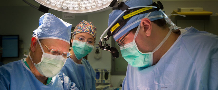 Masked faces of three surgeons at work in OR
