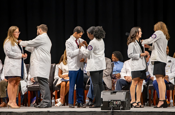 Medical students in white coats pin honor society pins on each other. 