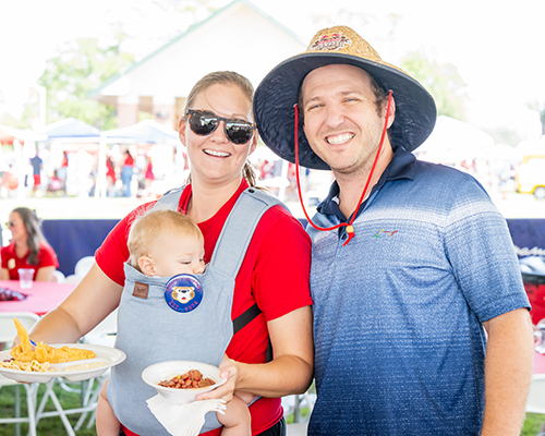 Couple smiling with their baby at tailgate event.