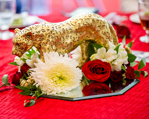 Golden jaguar statue on mirror plate surrounded by flowers.