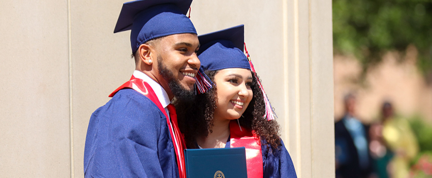 Two new graduates smiling holding diploma.