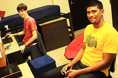 Two male students sitting in their dorm room playing video games