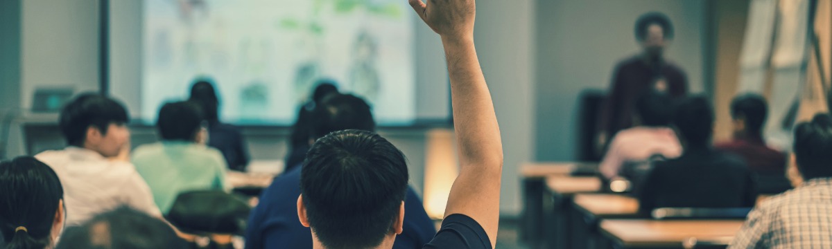 teacher at front of classroom full of students with one student raising their hand