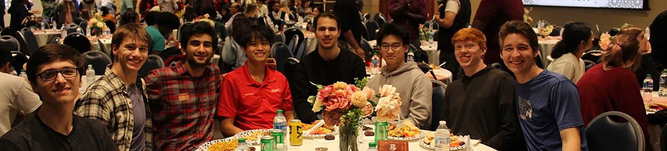 Group of students sitting at a round table eating at event.