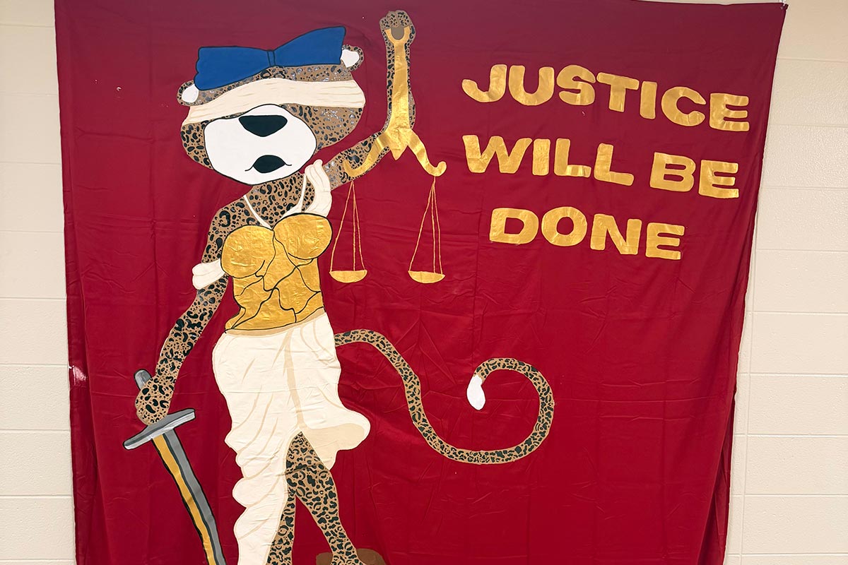Ms Pawla holding up weight of justice with text Justice will be done. Ms Pawla holding up weight of justice with text Justice will be done.