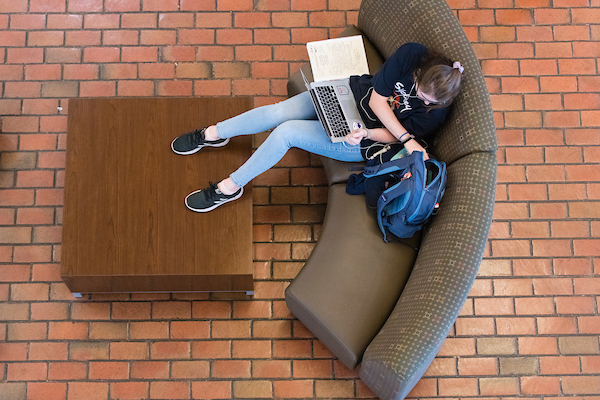 Student sitting on couch with laptop in their lap.