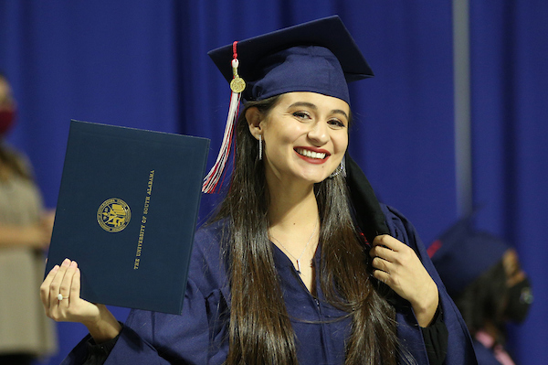 Student in cap and gown holding diploma smiling